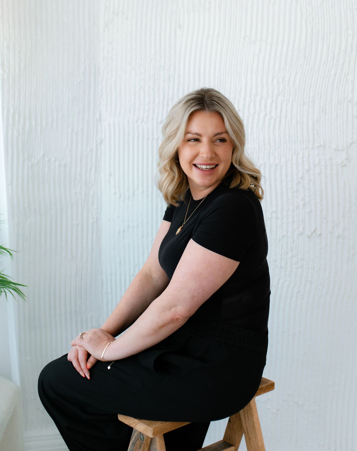 A person in a black dress poses gracefully on a wooden chair against a white background in a photo series.