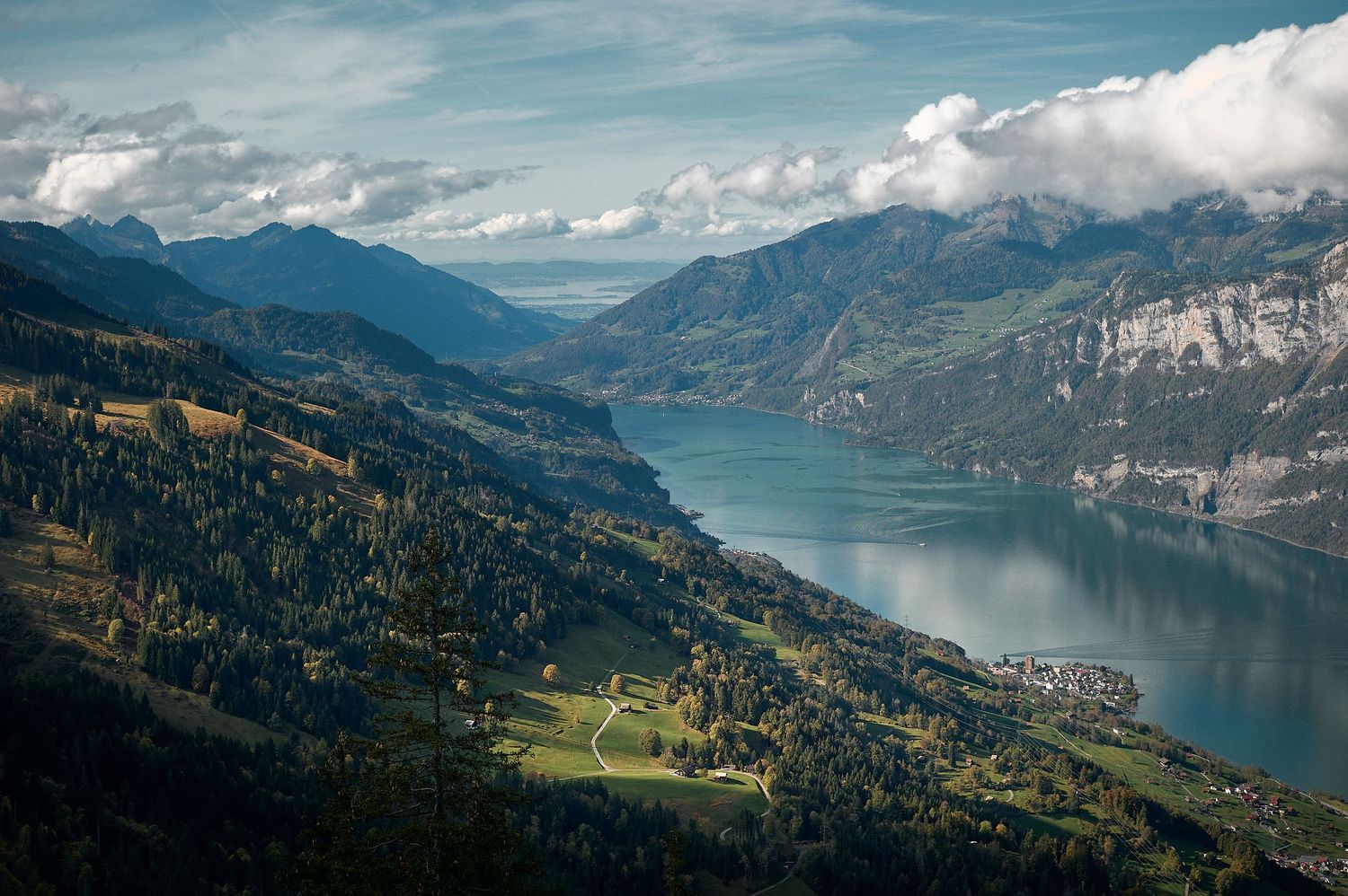 Aerial view of a turquoise alpine lake surrounded by steep mountains and green hillsides in Switzerland.
