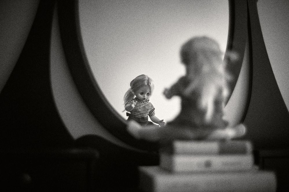 A black and white artistic photograph of decorative figurines with a reflection in a mirror creating a dreamy effect.