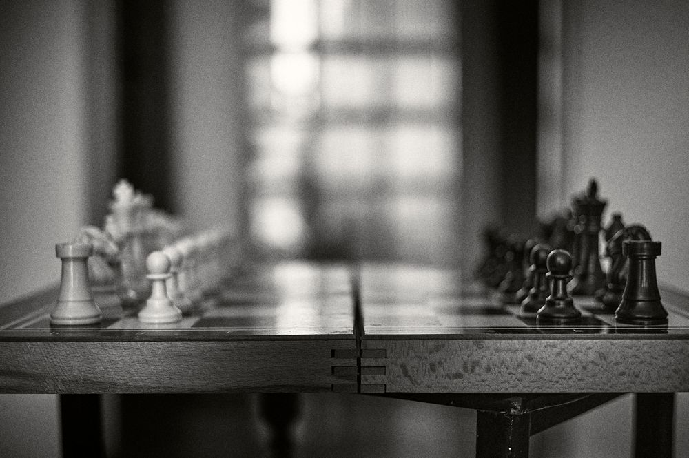 A black and white chess board setup with pieces arranged for a game, illuminated by soft window light.