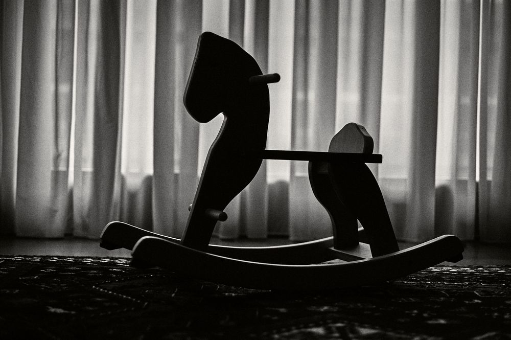Black and white silhouette of a person practicing yoga poses in front of a window with vertical blinds.