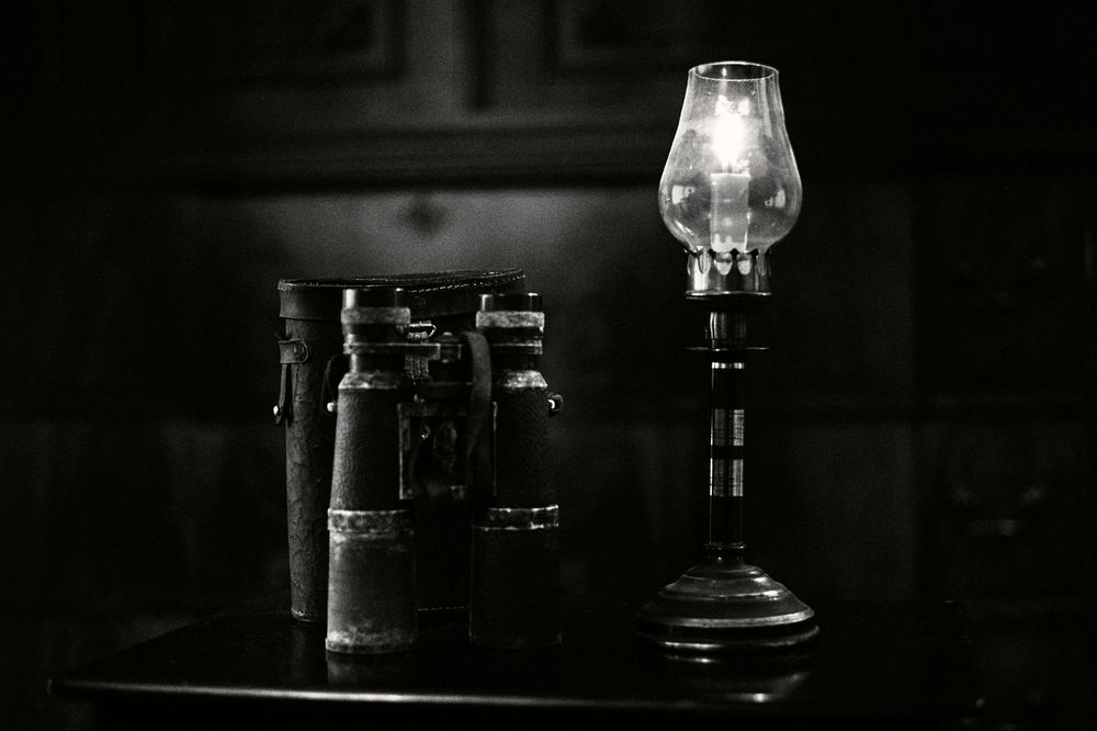 A dark and moody bar counter with empty glassware and bottles silhouetted against dim lighting.
