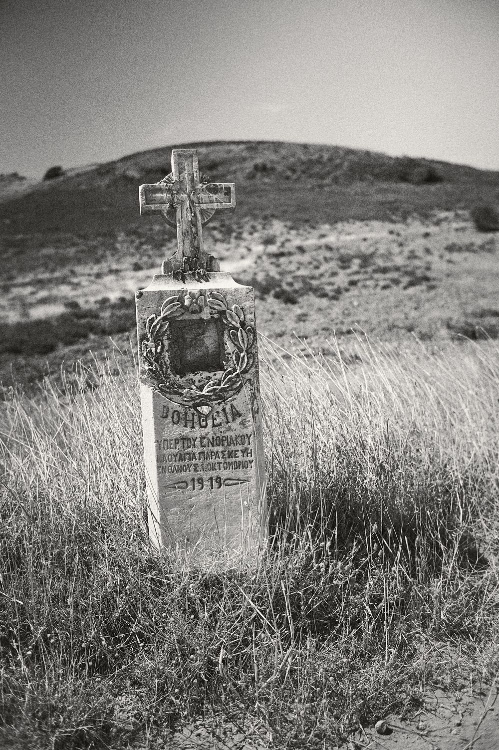 A series of black and white photographs showing old wooden crosses and grave markers in a grassy field on a hillside.