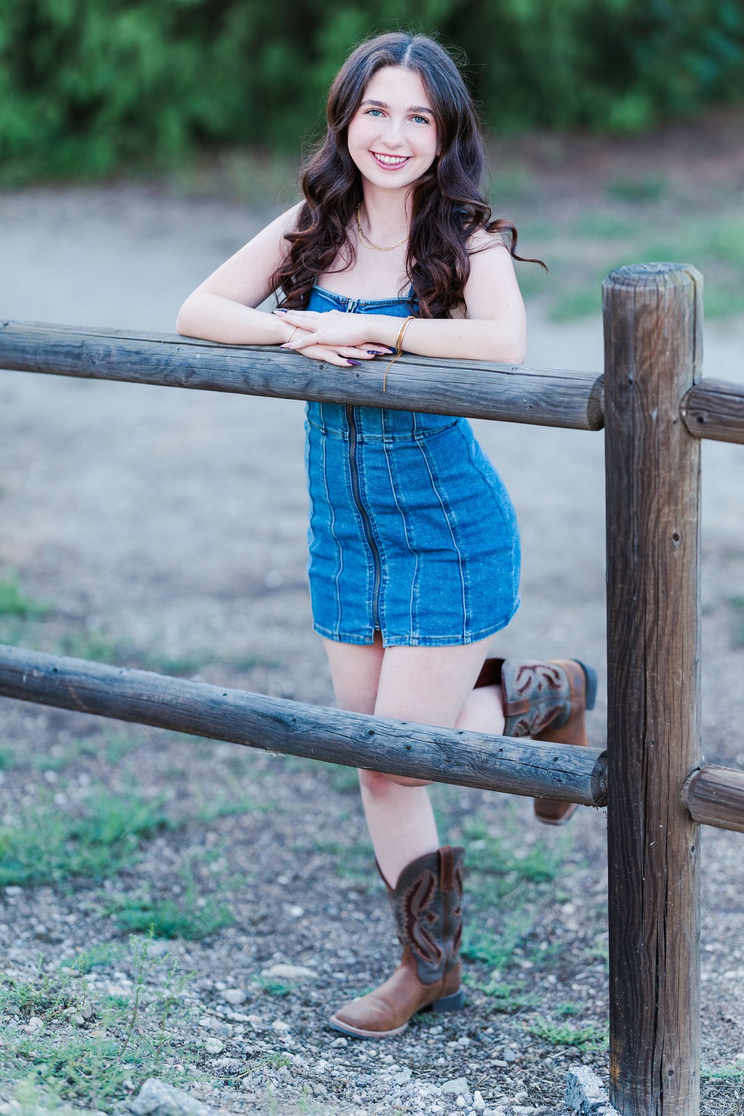 Someone in a blue dress sits barefoot on a large rock by a peaceful stream in a natural outdoor setting.