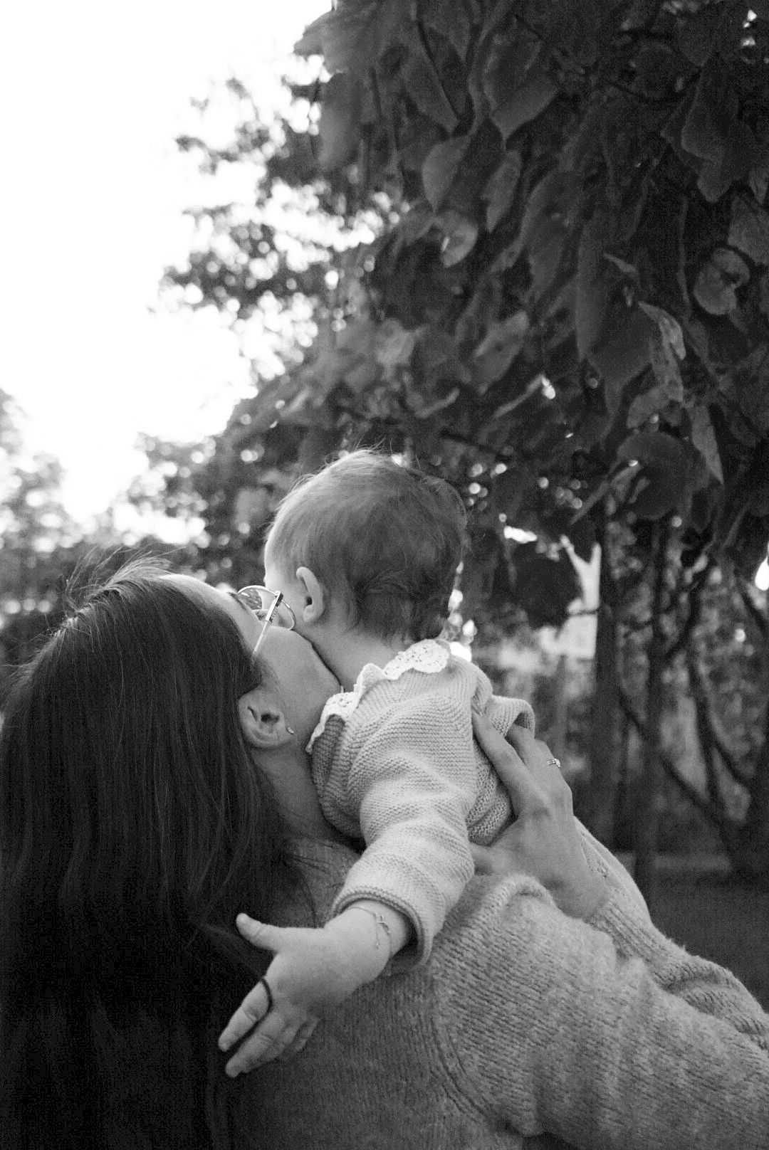 Tender moment between parent and baby captured in black and white against natural foliage.