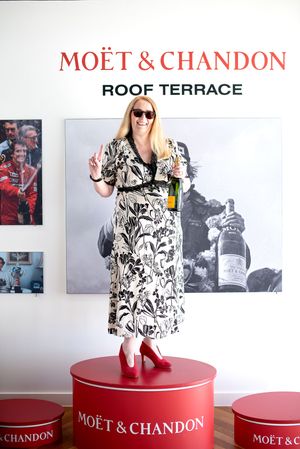 Woman in floral dress holding Moët & Chandon champagne bottle, standing on red branded cylinder at Roof Terrace.