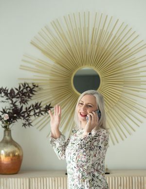 Person in floral print top poses playfully near decorative sunburst mirror and wall decor.