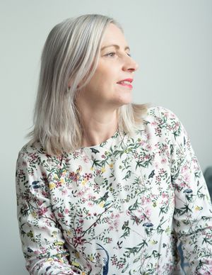 Person in a floral print sweater with silver hair looking to the side against a light background.