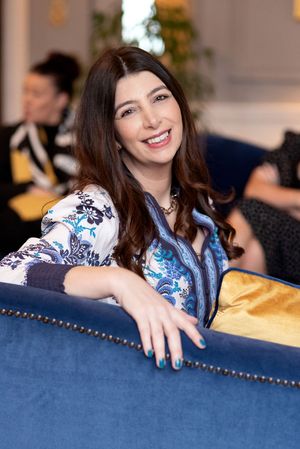 Person in a floral print blouse relaxes on a blue upholstered couch at a social gathering.