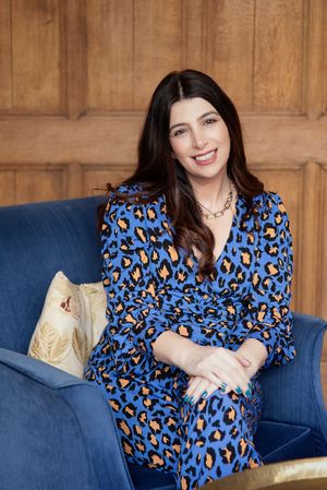 Woman relaxes on blue couch wearing vibrant blue leopard print top with decorative throw pillows.