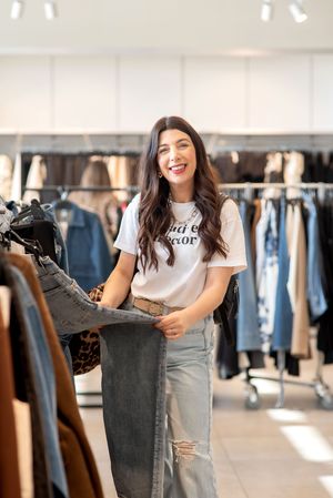 Woman working in clothing retail store handles denim merchandise while smiling.