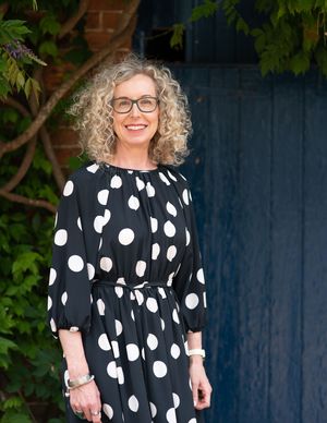 A polka dot dress in black and white with short sleeves is shown against a dark blue wall with greenery.