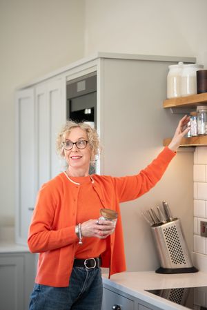 Person in bright orange cardigan making enthusiastic gestures in modern kitchen setting.