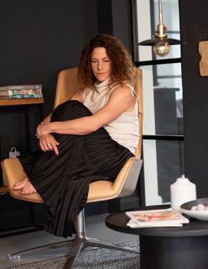 Person in black dress and white top lounging in modern wooden chair.