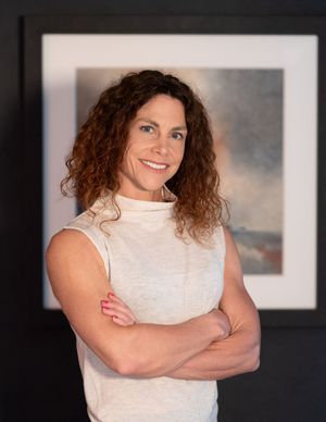 A cream-colored turtleneck top is styled against a dark background with framed artwork.
