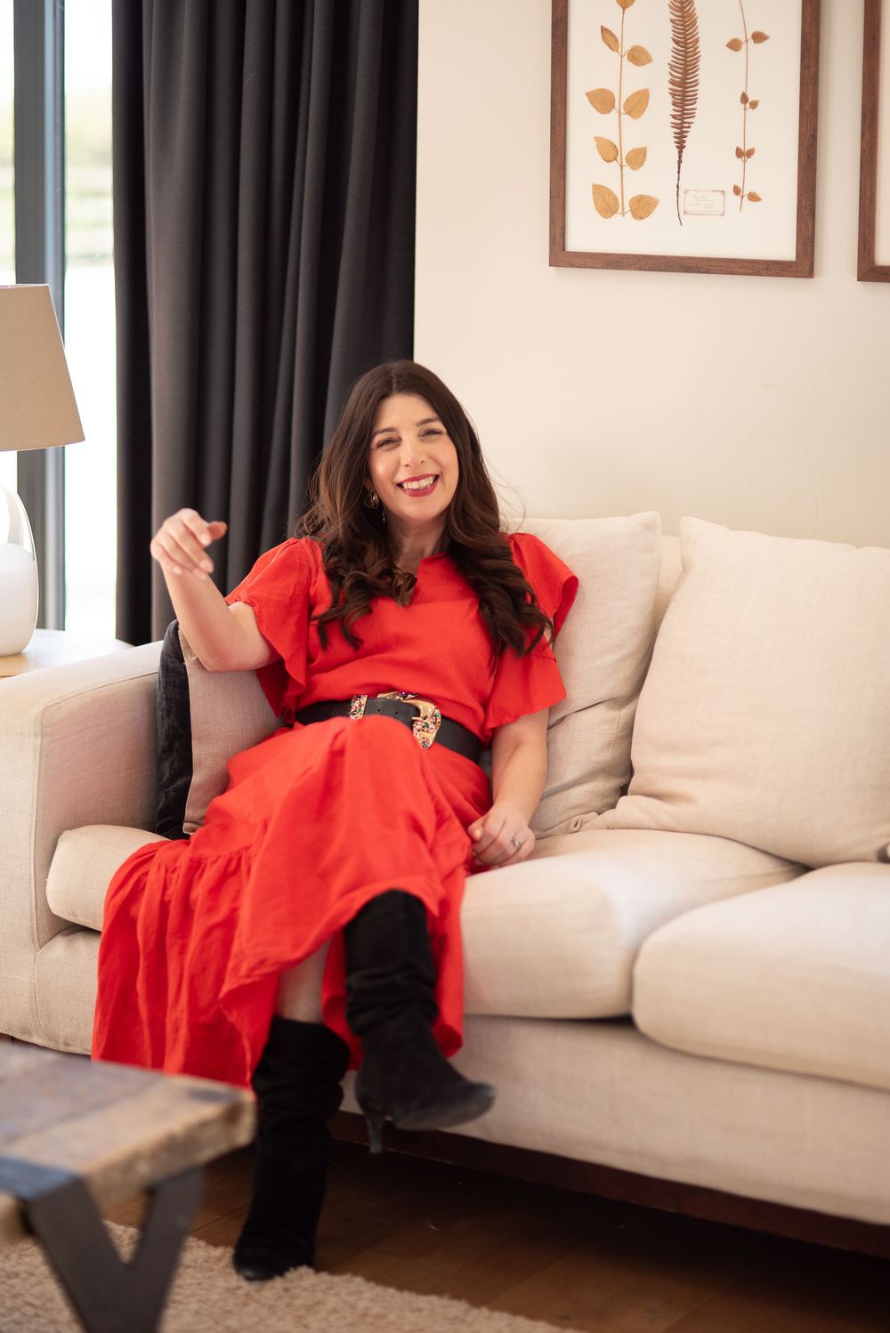 Woman in bright red dress lounges casually on a beige couch in a modern living room setting.