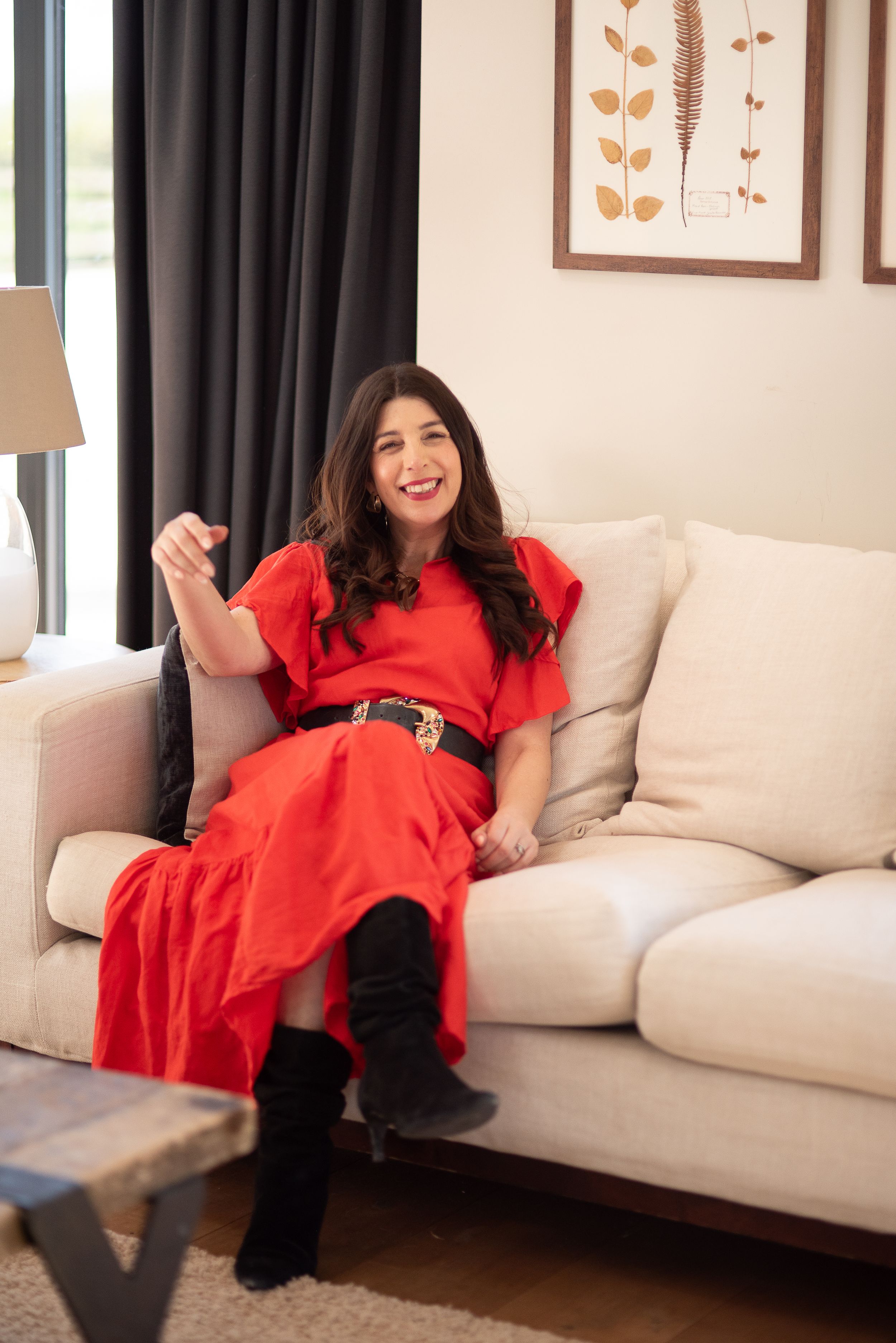 Woman in bright red dress lounges casually on a beige couch in a modern living room setting.