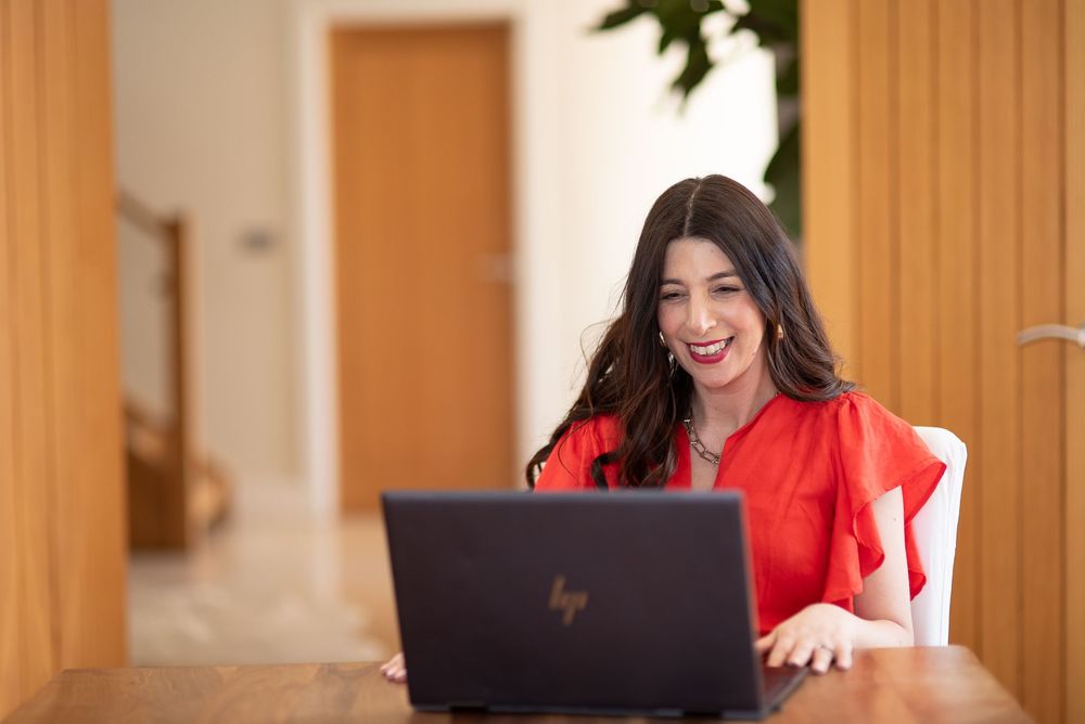 A person in a bright red blazer sits at a desk in a professional office setting.