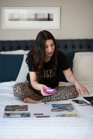 Person in black top and leopard print pants relaxing on white bed with magazines.