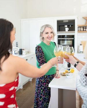 Women toasting with wine glasses in a modern white kitchen, smiling and celebrating together.
