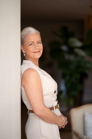 Professional in a sleeveless white outfit posing confidently against a neutral background.