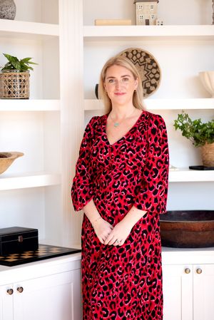 Person wearing red leopard print dress poses in modern white kitchen with built-in shelving.