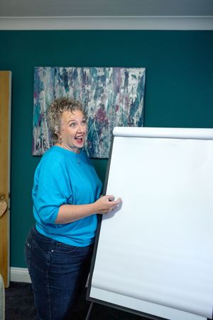 Person in bright turquoise shirt stands by whiteboard in teal-walled room during presentation.