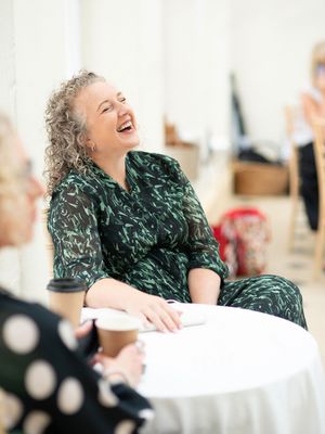 Person in green patterned dress laughing while seated at white table.