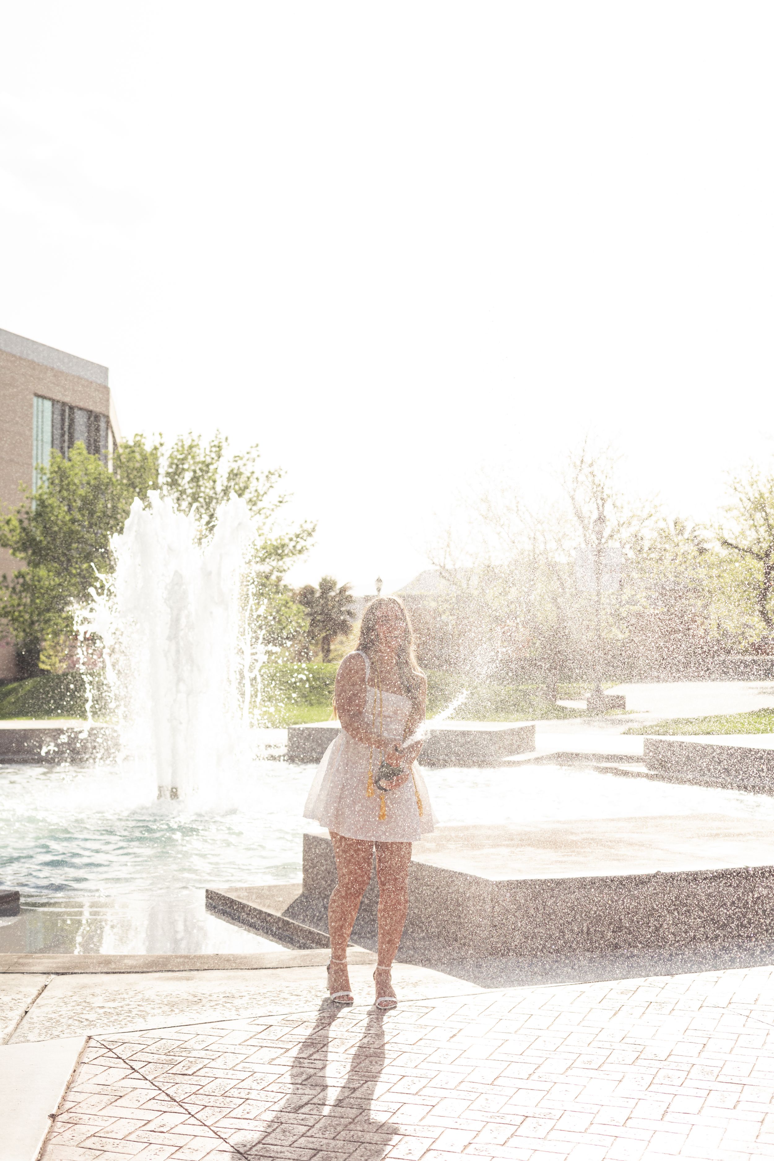 Child playing and running through water sprays at an outdoor fountain on a sunny day.