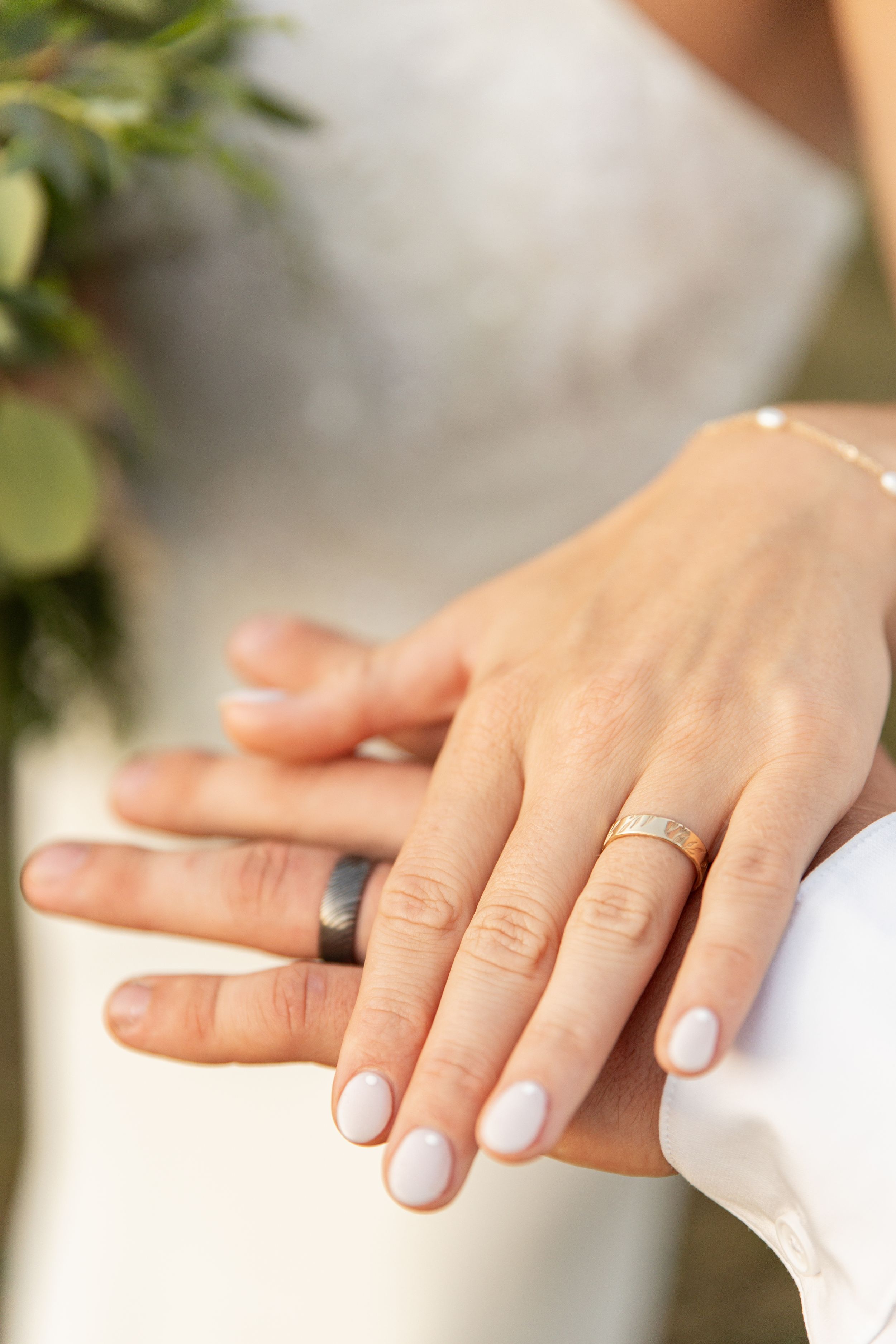Close-up view of hands wearing white nail polish and delicate rings against a soft blurred background.