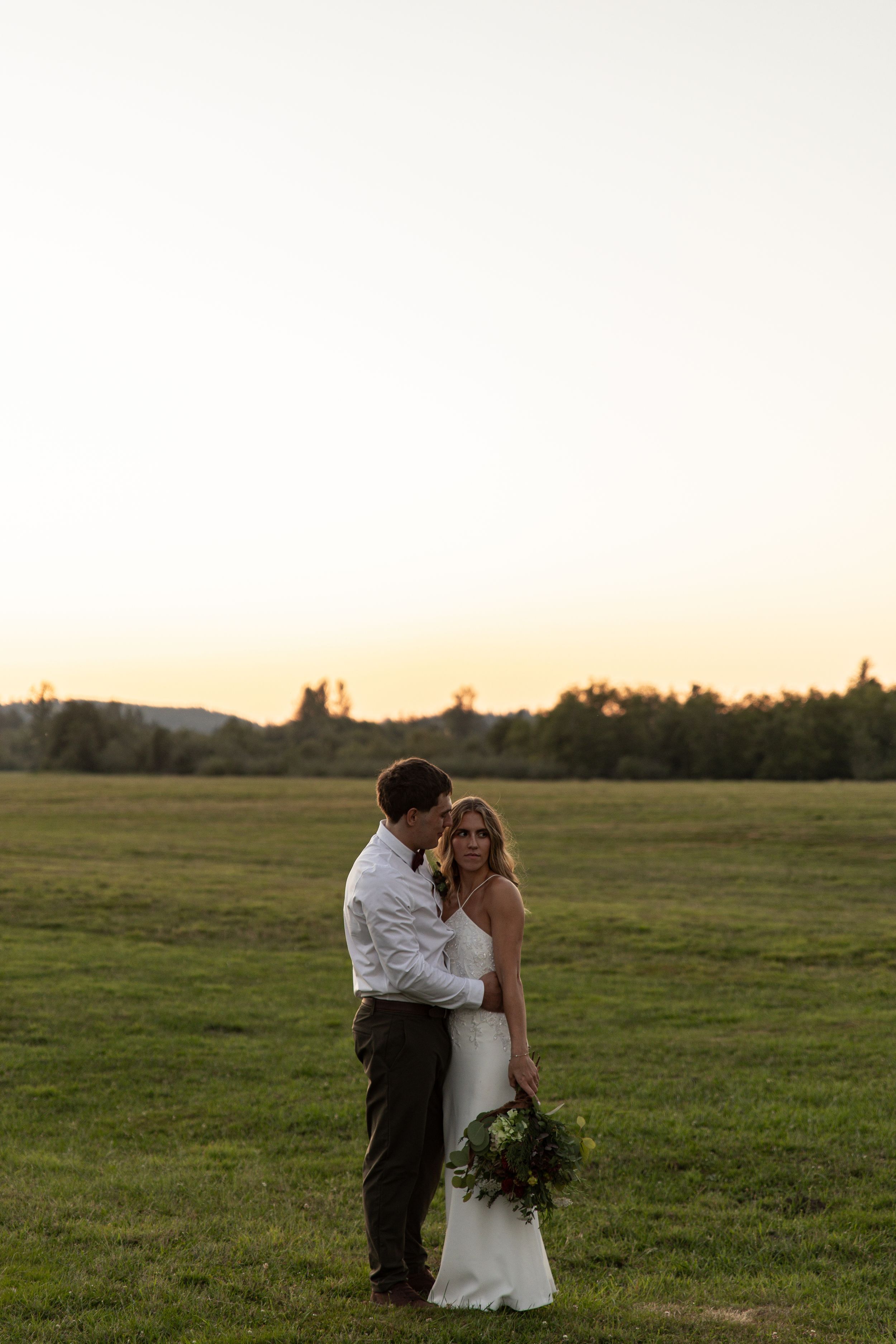 A romantic couple embraces in a golden field at sunset during their wedding photoshoot.