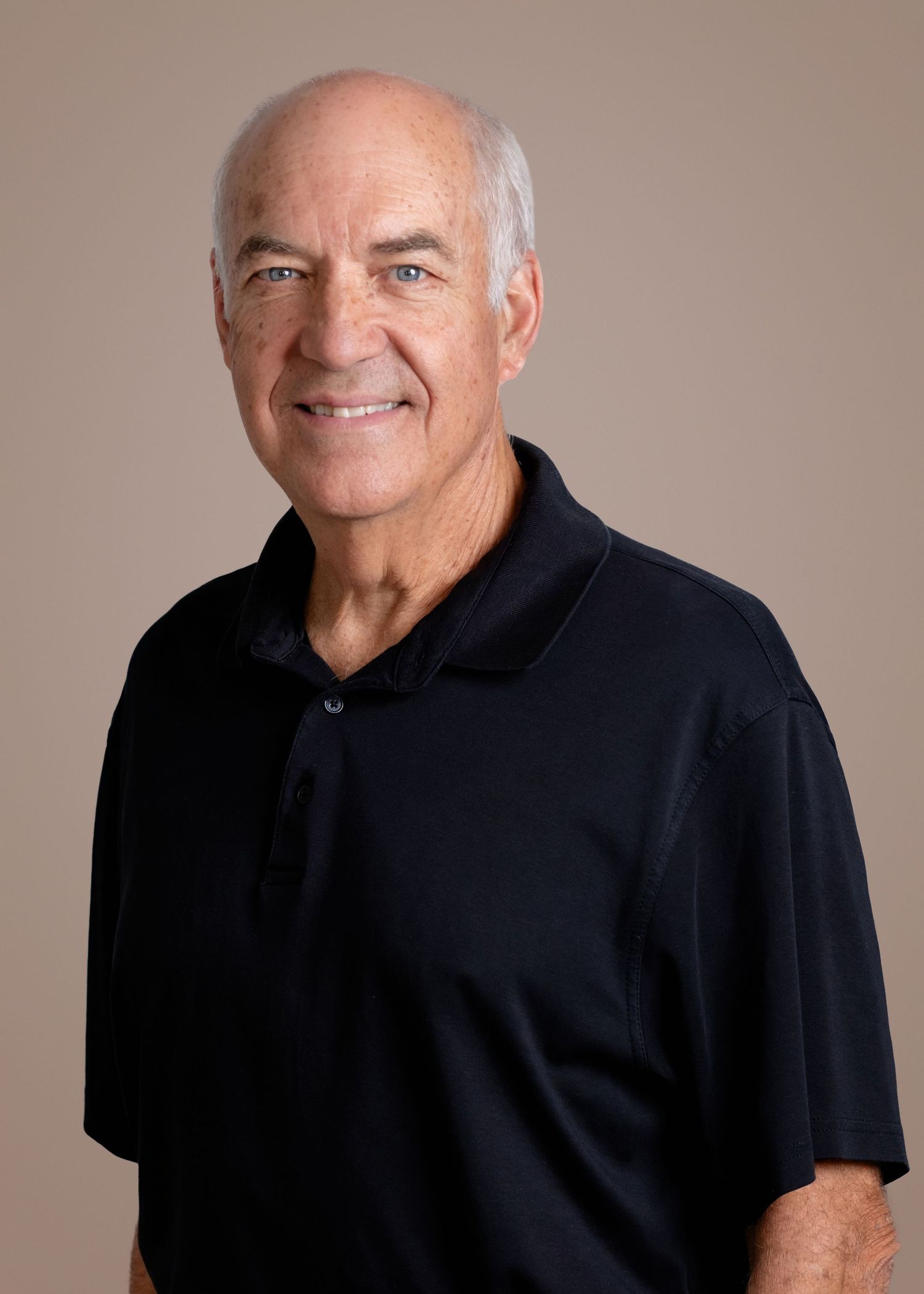 Person wearing glasses and a bright blue zip-up fleece with Calvary branding smiles warmly against dark background.