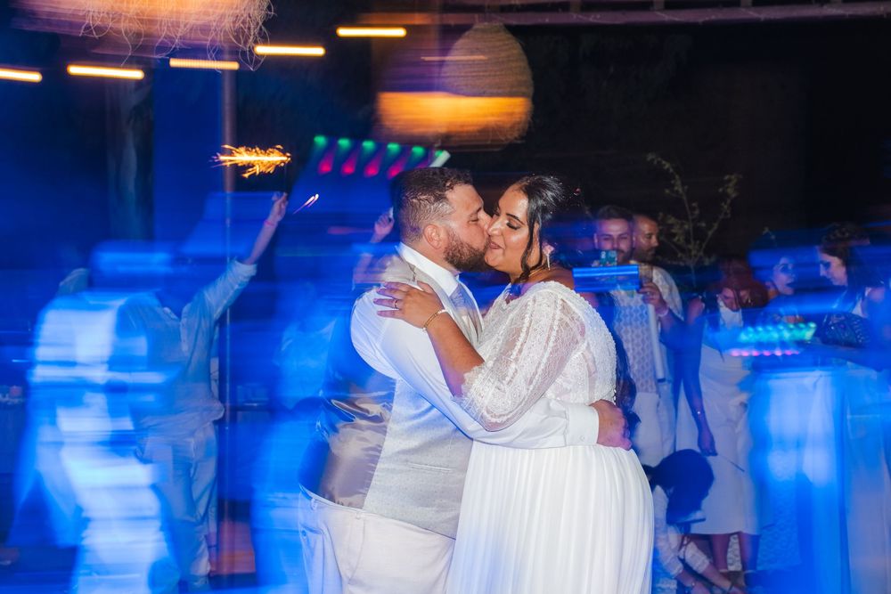 Bride and groom sharing a passionate kiss on the dance floor surrounded by blue lights during their wedding reception.