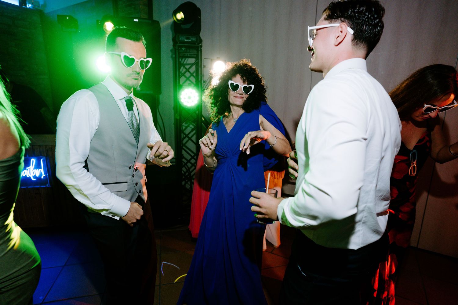 Dancers move to the music under vibrant green lighting at a festive indoor party.