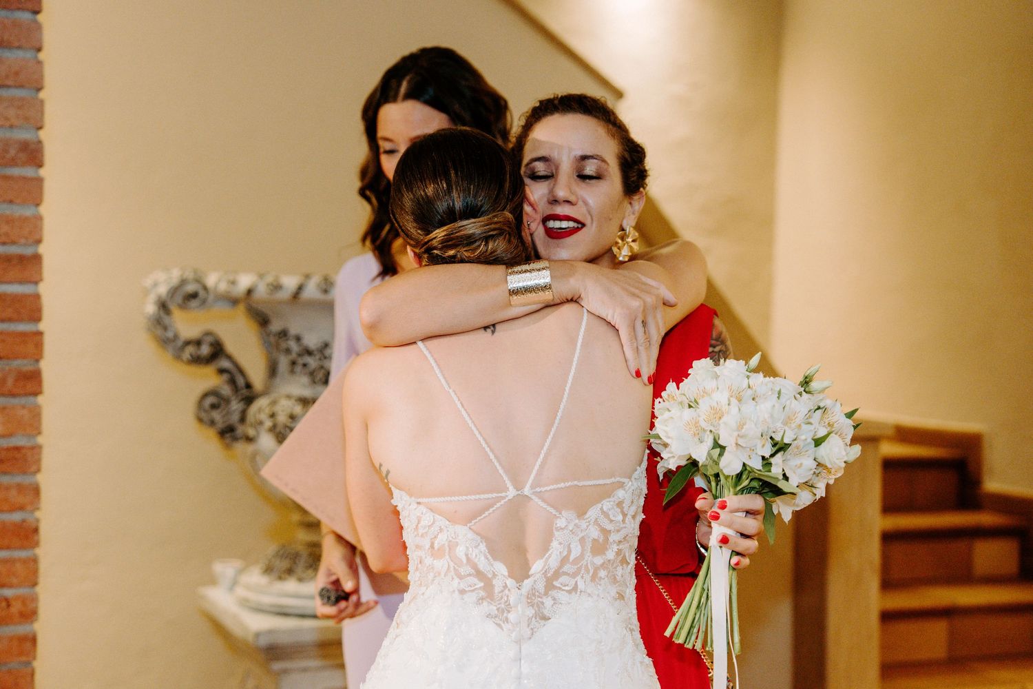 Joyful wedding party moment captured in warm-toned hallway with white floral bouquets.