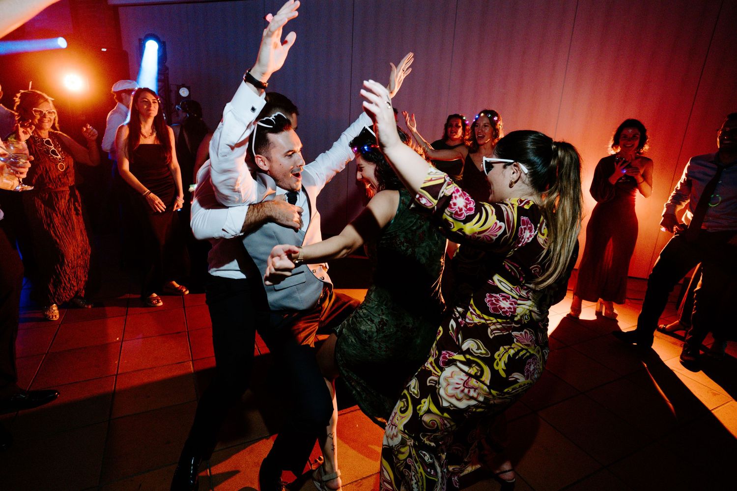 Dance floor filled with celebrating guests under dramatic red and orange lighting effects.