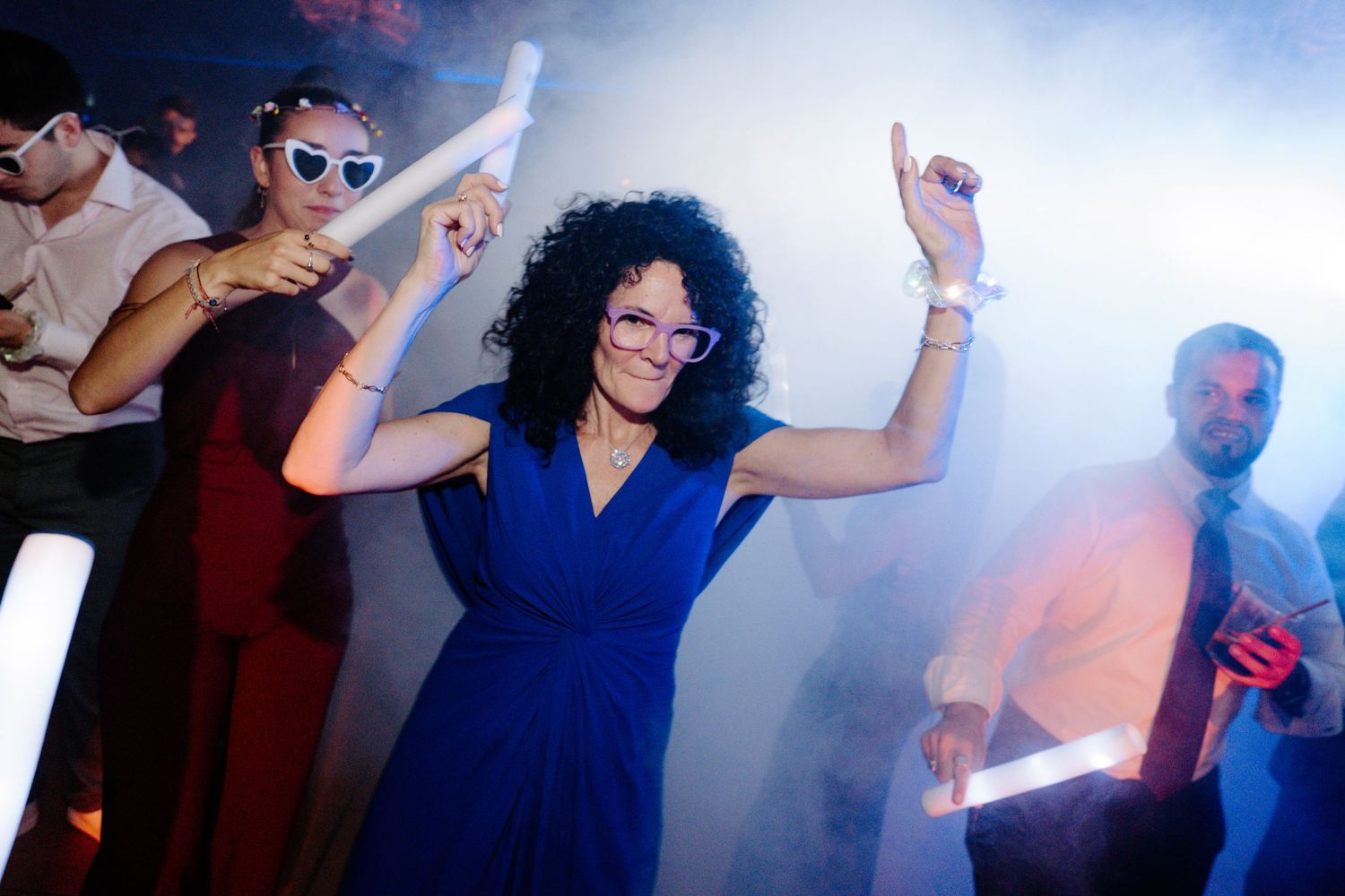 Party guests dancing under bright blue spotlights at an indoor celebration.