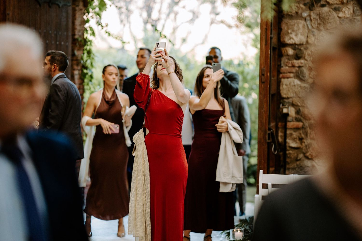 Wedding party and guests gathering in a rustic stone archway venue.