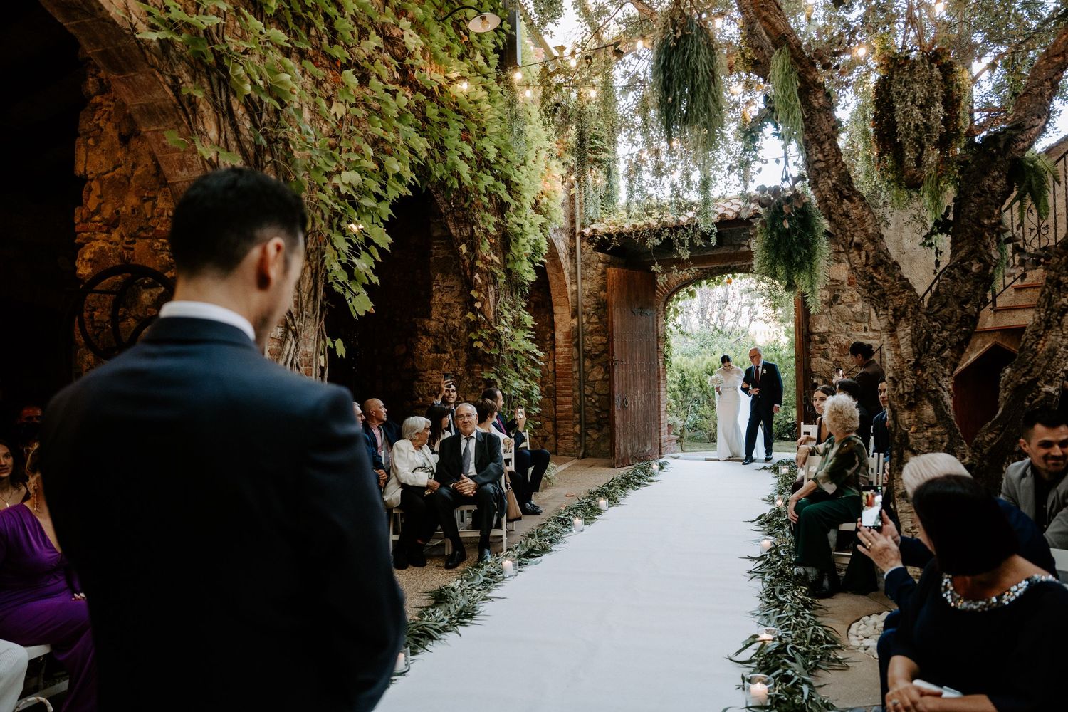 Wedding guests walking through a stone archway corridor with natural lighting.
