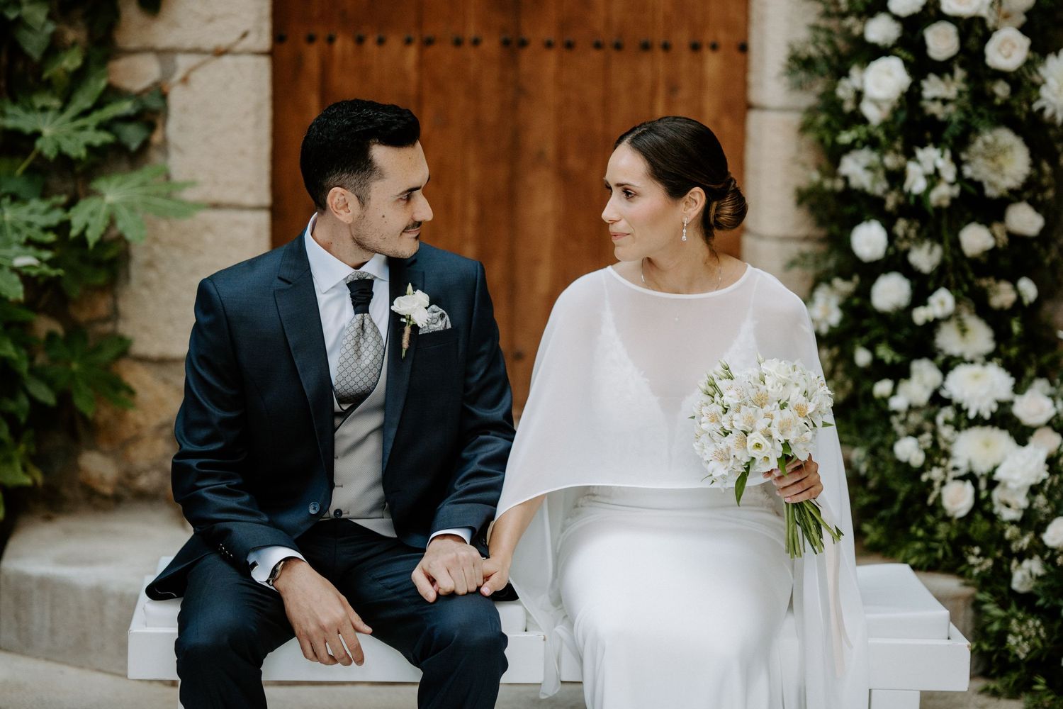 Romantic wedding ceremony scene with white floral arrangements and ivy-covered walls.