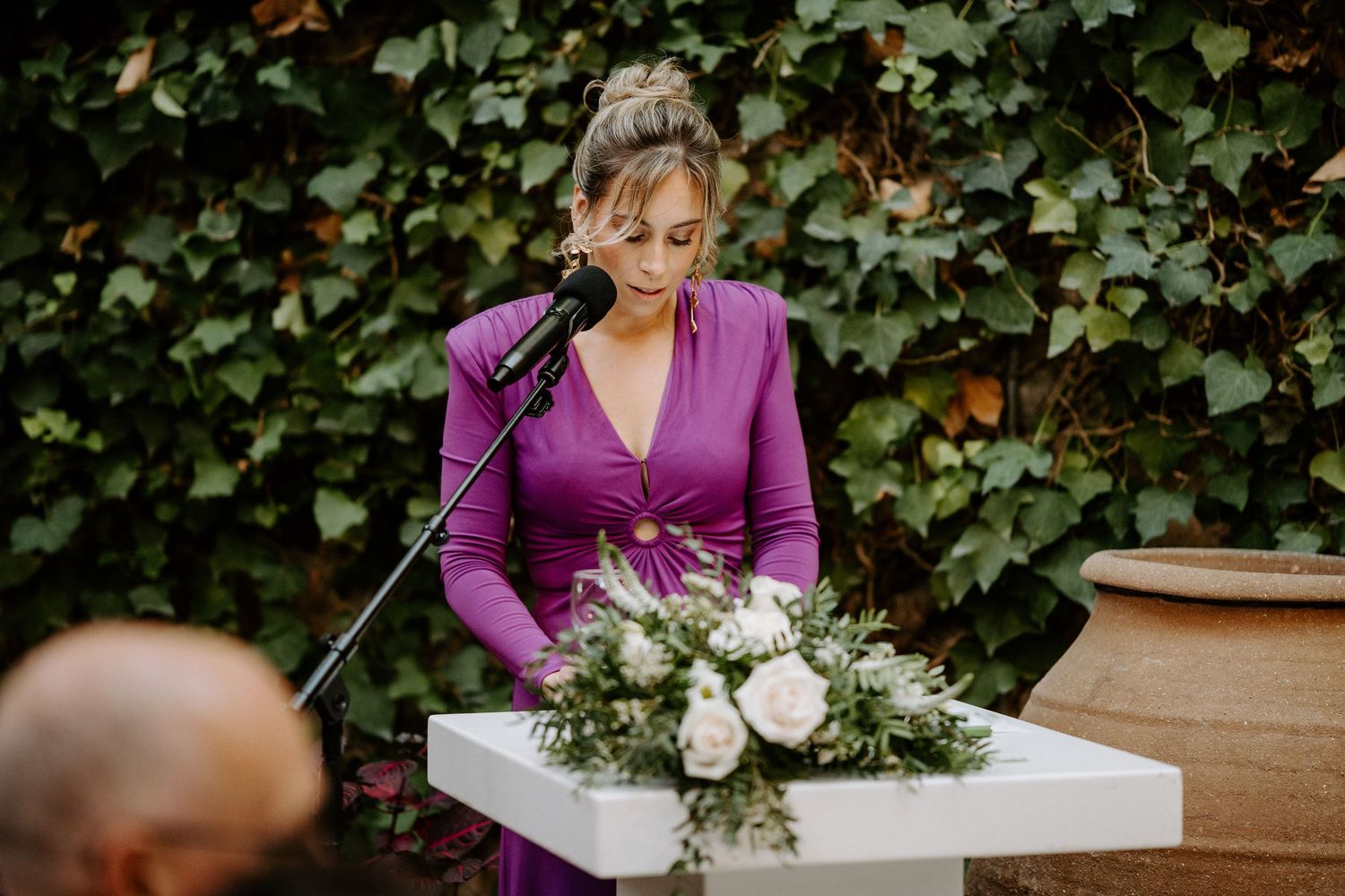 Wedding ceremony speakers delivering heartfelt messages at white podium with floral decorations.