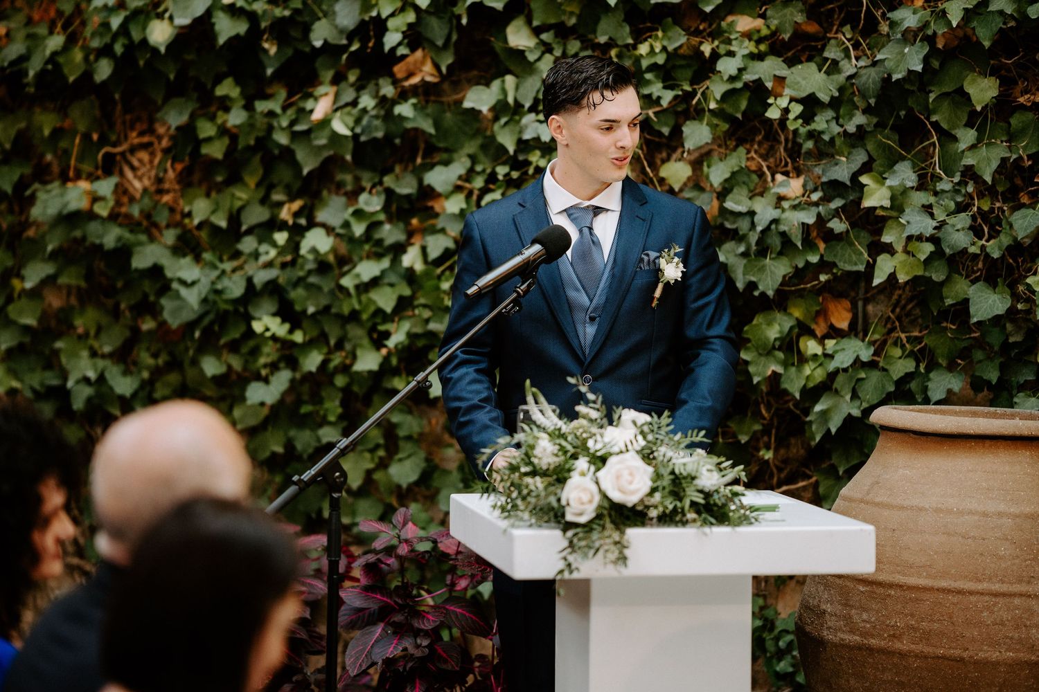 Outdoor wedding ceremony with elegant white floral arrangements and natural ivy backdrop.