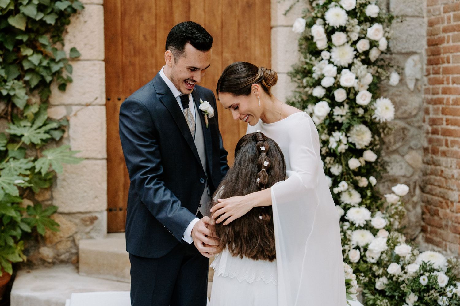 A tender moment between a couple during their wedding ceremony beside white floral arrangements.