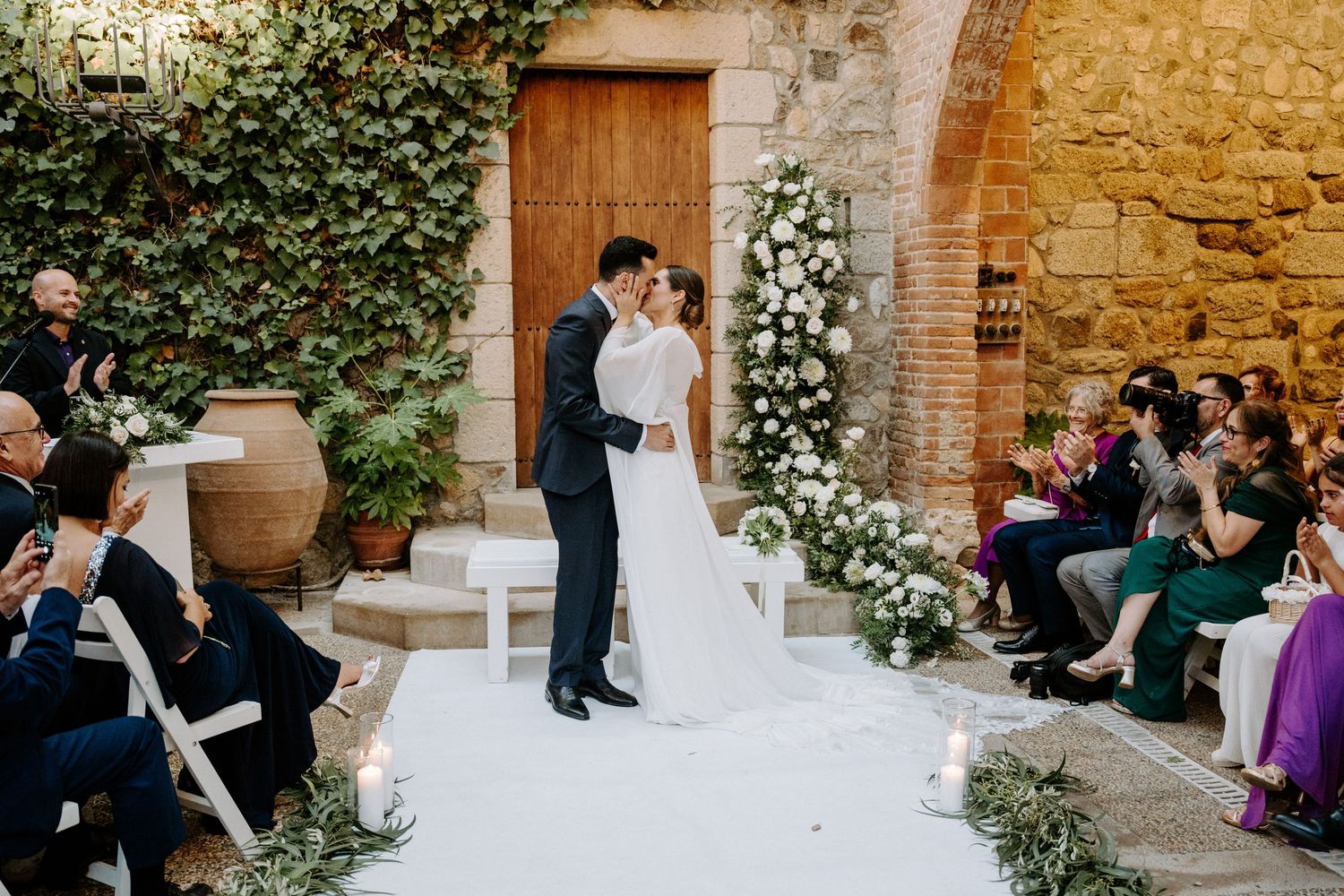 Wedding celebration in a rustic stone courtyard with ivy-covered walls and wooden doors.
