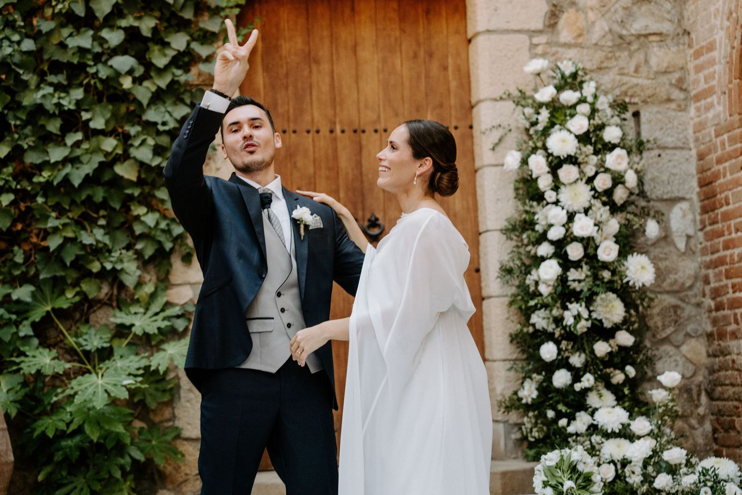 Intimate wedding moment captured in front of rustic wooden door with white floral decorations.