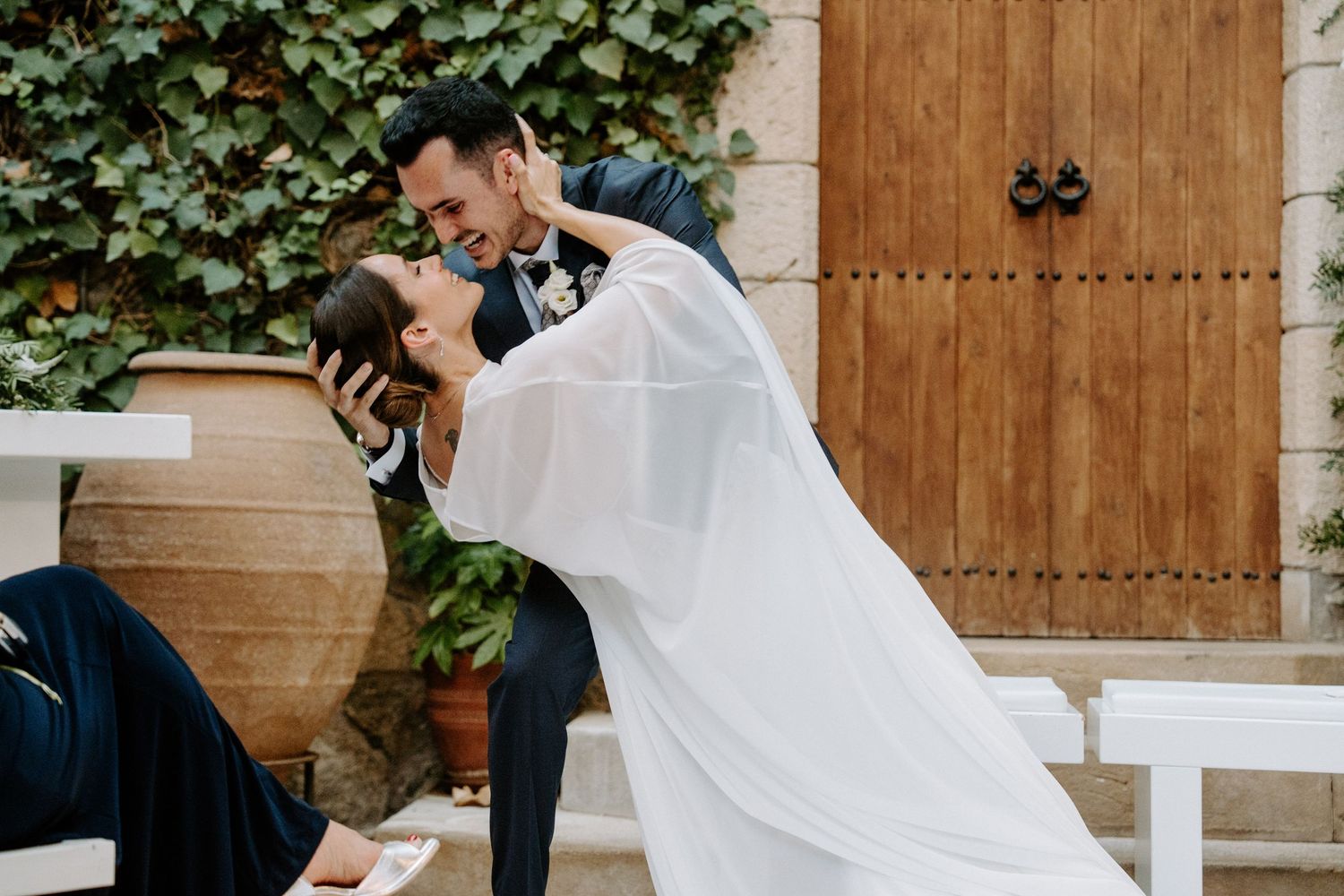 La pareja de novios comparte un momento romántico en un patio ajardinado con paredes de piedra y hiedra trepadora. Mas de Sant Llei