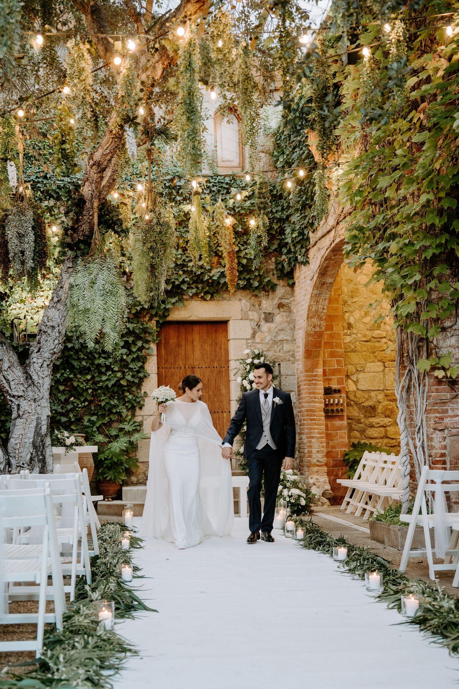 Garden wedding venue with string lights, white chairs, and natural stone architecture.