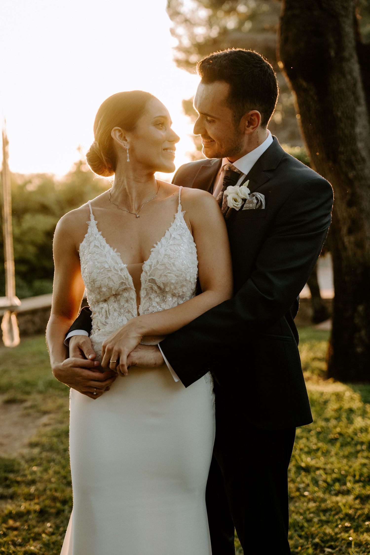 A romantic sunset wedding portrait featuring an elegant lace dress and classic black tuxedo.