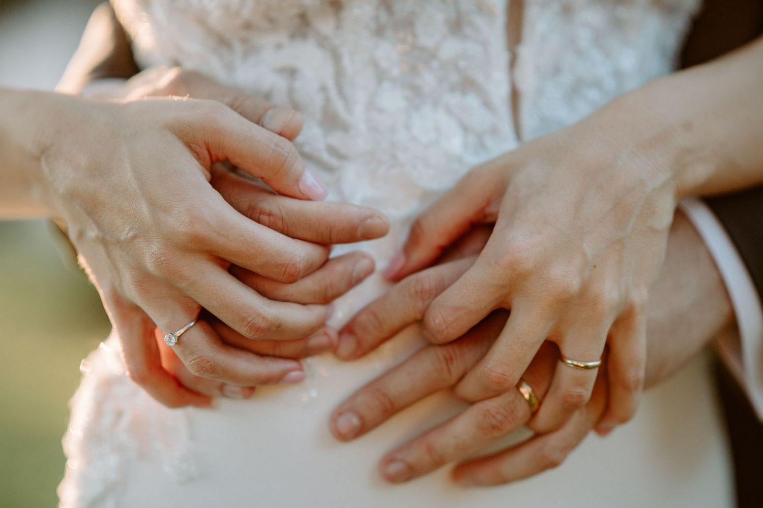 Close-up detail of hands showing off a wedding ring against delicate white lace fabric.