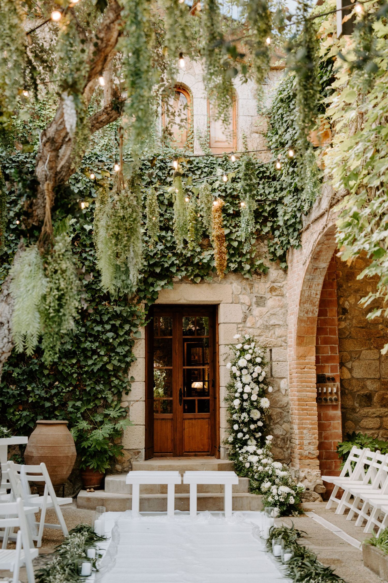 Stone archway venue decorated with cascading ivy and white chairs for ceremony.